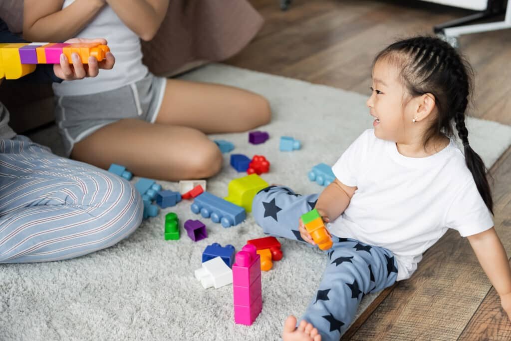 parents playing building blocks with happy asian daughter