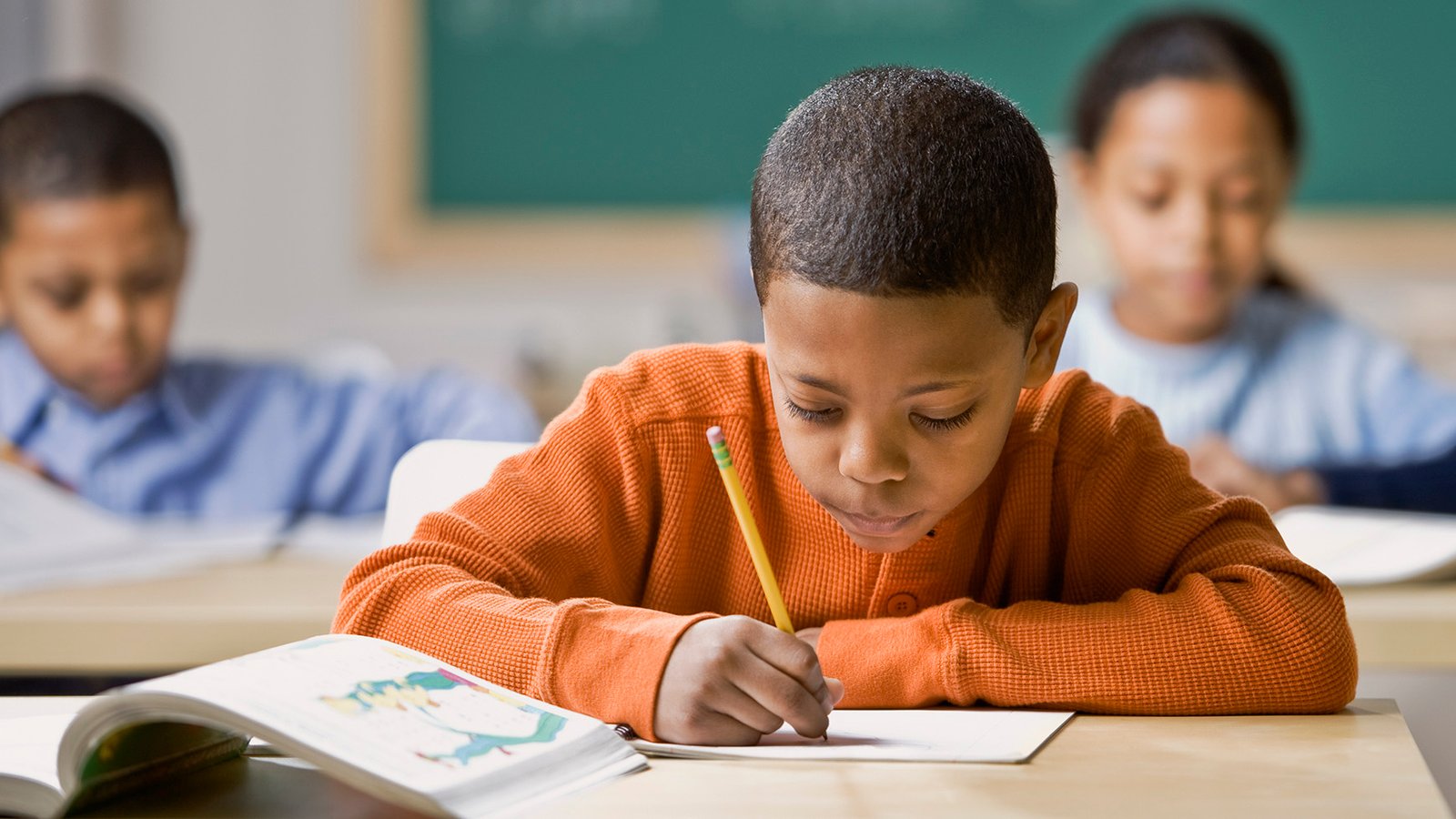 Mixed Race boy writing at school desk Mixed Race boy writing at school desk
